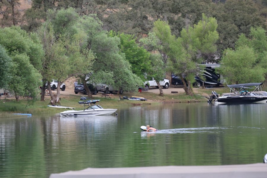 A paddler crossing calm water past lakeside campsites and boats