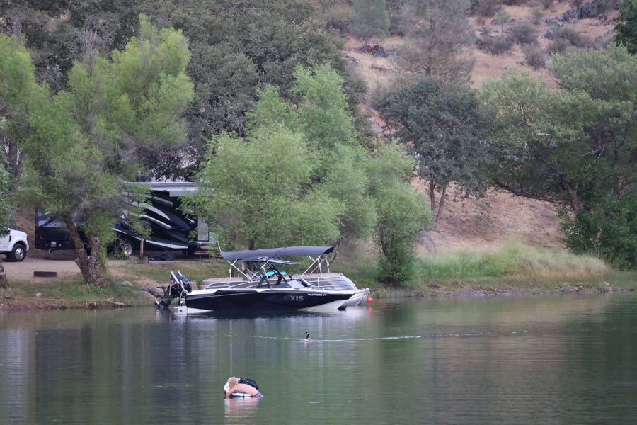 A wake boat moored in front of a lakeside campsite