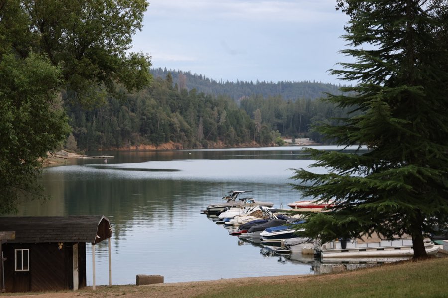 A wide view of Rollins Lake with boats moored along the shore and forested hills beyond