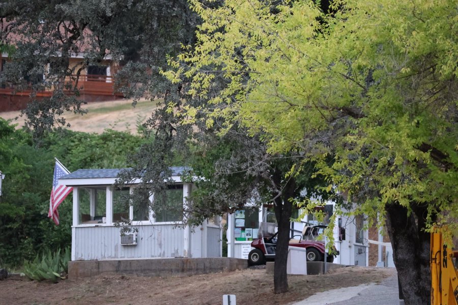 The Greenhorn gatehouse with an American flag and a golf cart under the oaks
