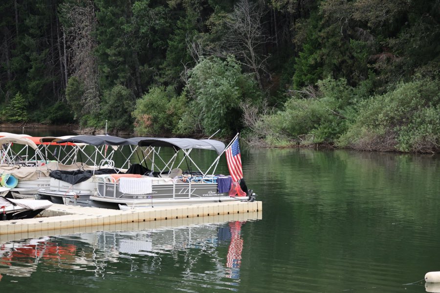 Pontoon boats with canopies moored at a dock flying a small American flag on a calm lake