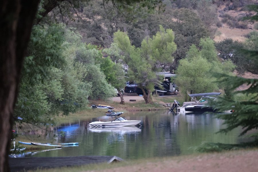 Boats pulled up along a tree-lined lake cove with campsites behind