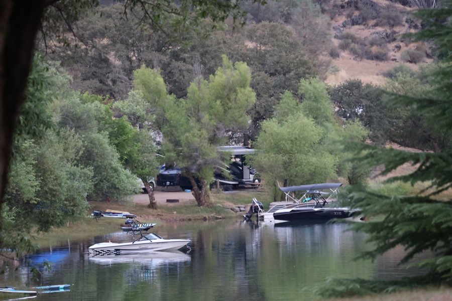 A wake boat and moored boats in a calm tree-lined cove near campsites