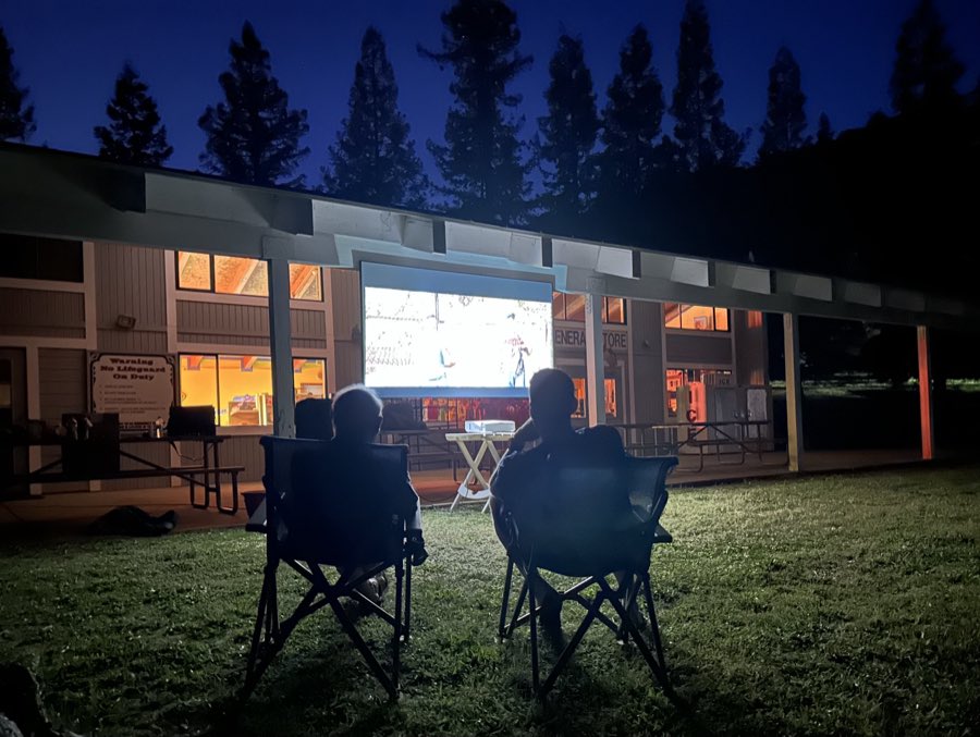Two people in camp chairs on a lawn at night watching an outdoor movie at the lodge