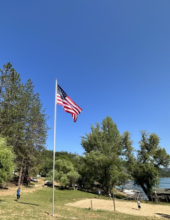 An American flag flying on a tall flagpole above the campground lawn near the lake