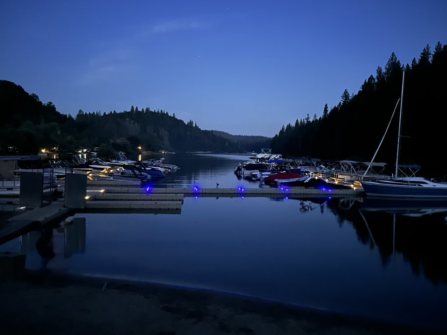 Docks with blue lights and moored boats on a still lake at twilight