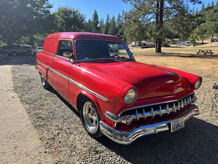 A restored red vintage sedan delivery car parked on the campground road