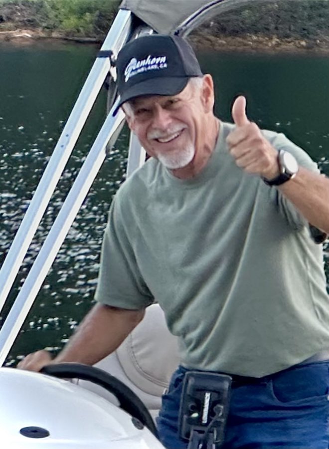 A smiling man in a Greenhorn cap giving a thumbs up at the helm of a pontoon boat