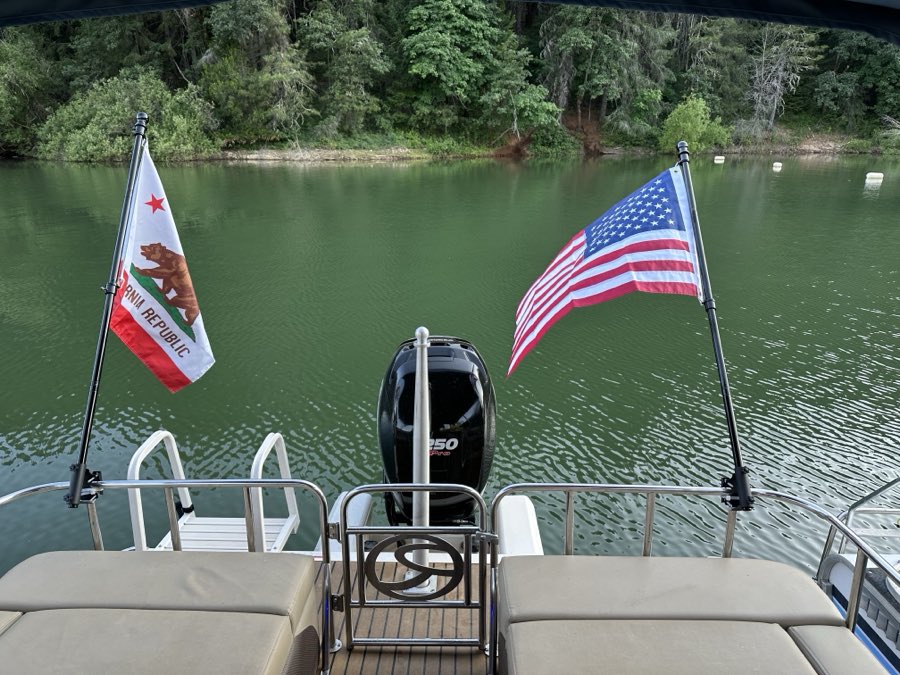California and American flags flying off the stern of a pontoon boat over calm water